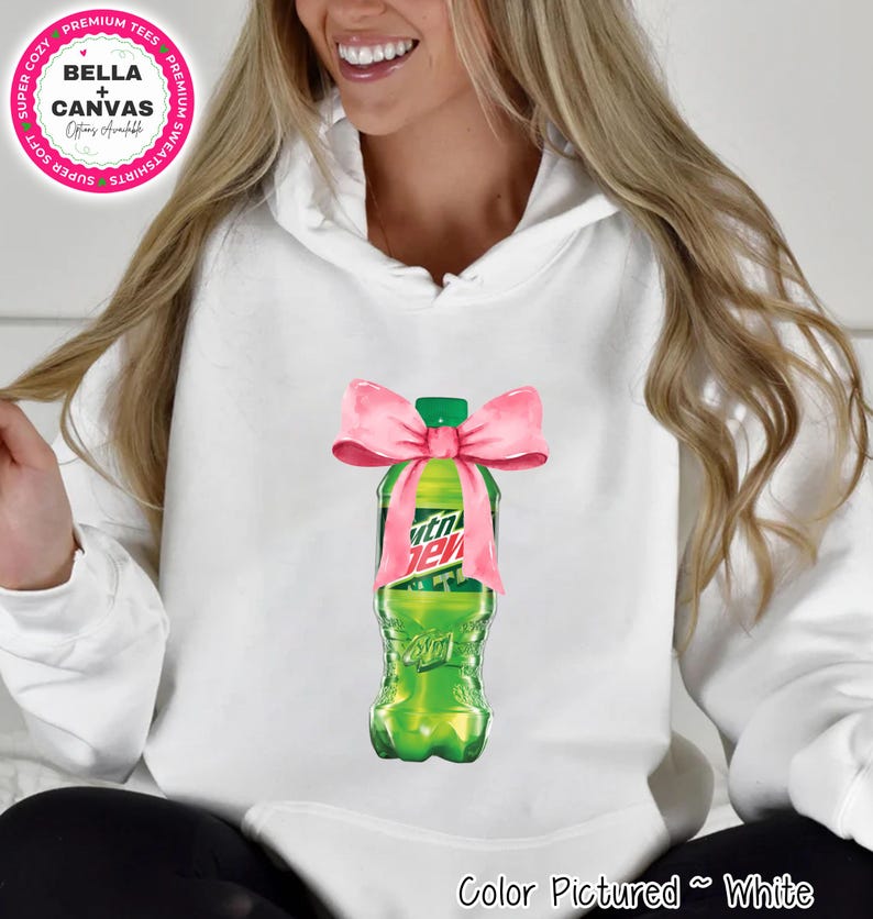 White hoodie with a graphic of a green soda bottle tied with a pink bow. The soda bottle has the text "Mtn Dew" on it. The hoodie has the text "BELLA + CANVAS" and "Color Pictured ~ White".