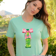 Mint green t-shirt featuring a graphic of a Mountain Dew bottle tied with a pink bow. The text 