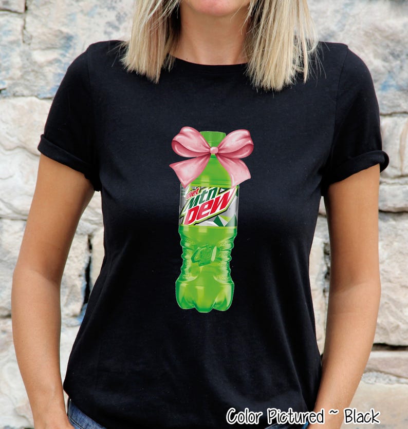 Black t-shirt featuring a graphic of a green Mountain Dew bottle tied with a pink bow. The Mountain Dew logo is visible on the bottle. The text "Color Pictured ~ Black" is at the bottom right.