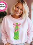 Pink sweatshirt featuring a graphic of a green Mountain Dew bottle tied with a pink bow. The sweatshirt has the text "Color Pictured ~ Pink" at the bottom. The Bella + Canvas logo is visible in the upper left corner.