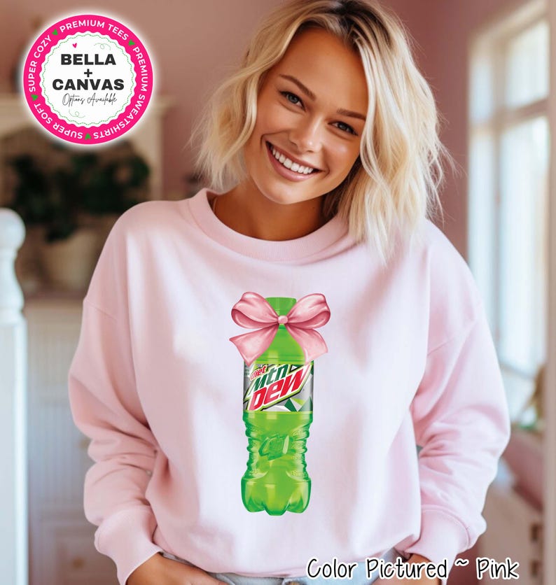 Pink sweatshirt featuring a graphic of a green Mountain Dew bottle tied with a pink bow. The sweatshirt has the text 