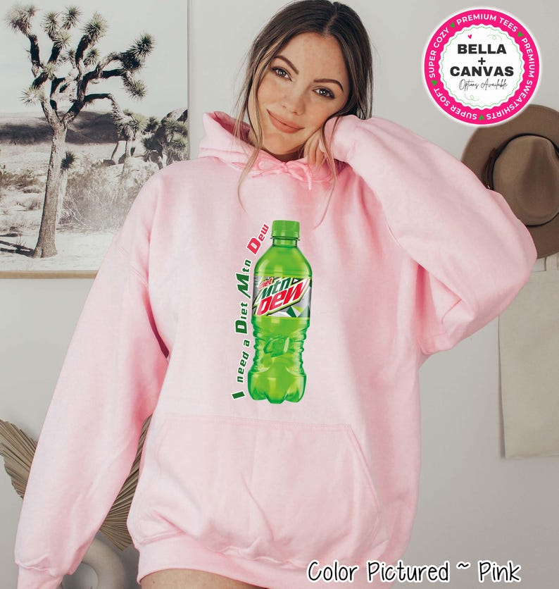 Pink hoodie with a Diet Mtn Dew graphic. The hoodie features a large graphic of a green Diet Mtn Dew bottle with the text "I need a Diet Mtn Dew" printed vertically on the left side. The Bella + Canvas logo is in the upper right corner.