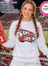 May include: A white long-sleeve sweatshirt featuring a graphic of a red marching band hat and two red pennants with the text GAME DAY. The design includes white stars and a white plume. A red foam finger with the number 1 is held to the side.