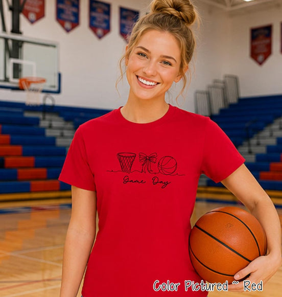 May include: A red short-sleeved t-shirt featuring a black line art graphic of a basketball hoop, a bow, and a basketball, with the text "Game Day" written in a cursive script below the illustrations. The shirt is a solid red color throughout.