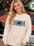 May include: An ivory long-sleeve sweatshirt featuring the word MOM in a black and white checkered pattern. The letter O is replaced by a blue wrestling headgear graphic, and two multi-colored star shapes are positioned over the center letters.