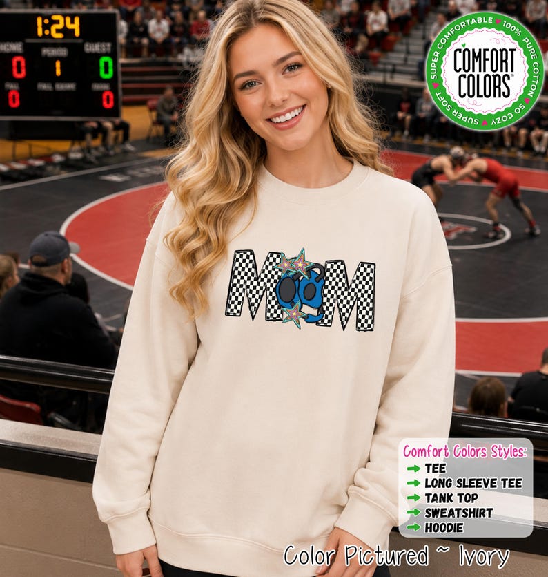 May include: An ivory long-sleeve sweatshirt featuring the word MOM in a black and white checkered pattern. The letter O is replaced by a blue wrestling headgear graphic, and two multi-colored star shapes are positioned over the center letters.
