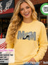 May include: A butter yellow long-sleeve sweatshirt featuring a graphic of the word MOM in a black and white checkered pattern. The letter O is replaced by a black and white winged shoe graphic surrounded by small teal and pink star illustrations.