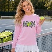 May include: A light pink long-sleeve sweatshirt featuring a graphic print of the word MOM with a checkered pattern, a tennis ball replacing the letter O, and colorful star accents. The garment is paired with a white pleated skirt.