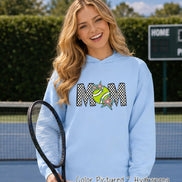 May include: A light blue hooded sweatshirt featuring a graphic design on the chest. The design displays the word MOM in a black and white checkered pattern, with a lime green tennis ball replacing the letter O and colorful star accents.