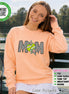 May include: A peach-colored long-sleeve sweatshirt featuring the text MOM in a black and white checkered pattern. The letter O is replaced by a lime green tennis ball graphic adorned with two colorful, multi-pointed star shapes.