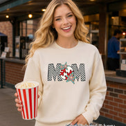 May include: An ivory crewneck sweatshirt featuring a graphic print of the word MOM in a black and white checkered pattern. The letter O is replaced by a red and white baseball design, accented with two colorful, multi-pointed star shapes.