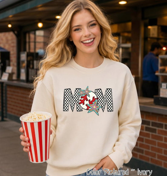 May include: An ivory crewneck sweatshirt featuring a graphic print of the word MOM in a black and white checkered pattern. The letter O is replaced by a red and white baseball design, accented with two colorful, multi-pointed star shapes.