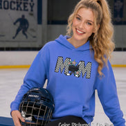 May include: A periwinkle blue hooded sweatshirt featuring a graphic on the chest that spells MOM in a black and white checkered pattern. The letter O is replaced by a black hockey puck and two crossed hockey sticks with colorful stars.