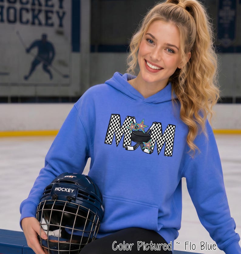 May include: A periwinkle blue hooded sweatshirt featuring a graphic on the chest that spells MOM in a black and white checkered pattern. The letter O is replaced by a black hockey puck and two crossed hockey sticks with colorful stars.