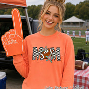 May include: A melon-colored long-sleeve sweatshirt featuring a graphic print of the word MOM in a black and white checkered pattern. The letter O is replaced by a brown football with white laces, accented by two colorful star shapes.