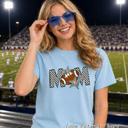 May include: A light blue short-sleeved t-shirt featuring a graphic print of the word MOM in a black and white checkered pattern. The letter O is replaced by a brown football with white laces, accented by two colorful star illustrations.