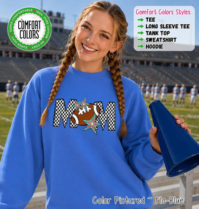 May include: A bright blue crewneck sweatshirt featuring a graphic print of the word MOM with a football replacing the letter O. The letters have a black and white checkered pattern, accented by two colorful star illustrations. Text reads Comfort Colors.