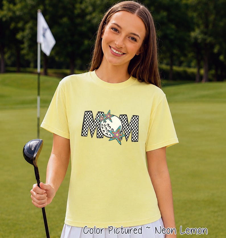 May include: A neon lemon yellow short-sleeve t-shirt featuring the word MOM in a black and white checkered pattern. The letter O is replaced by a white golf ball graphic, and two colorful star shapes are layered over the text design.