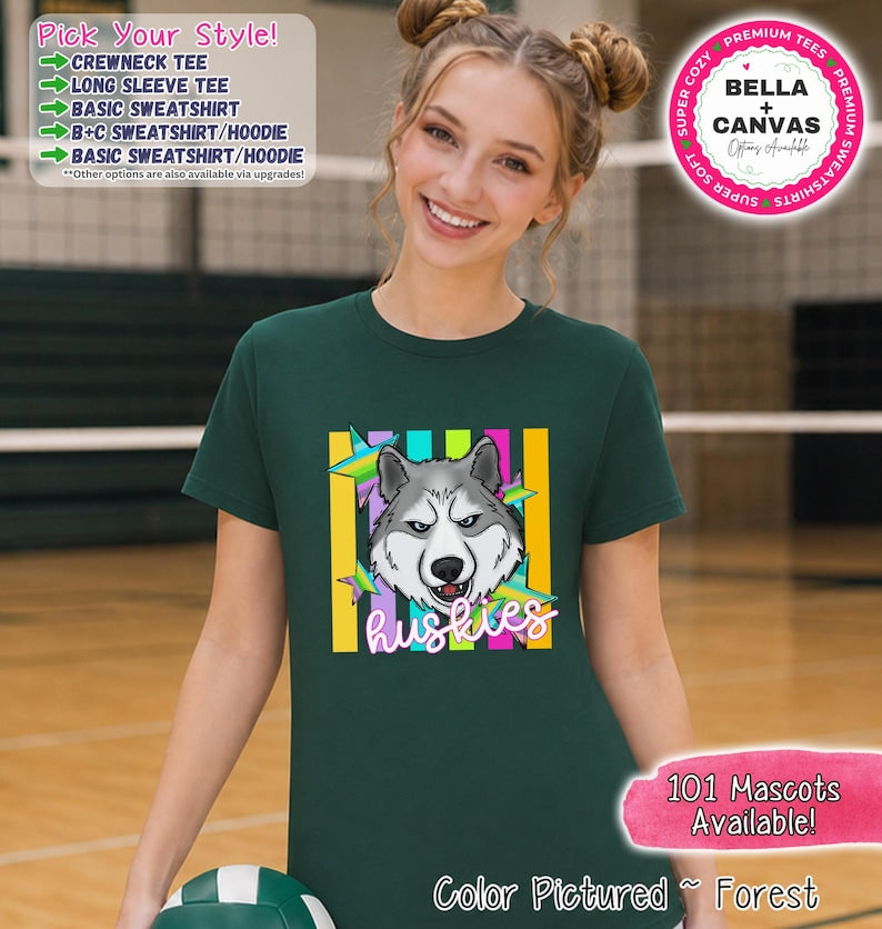 May include: A forest green short-sleeve crewneck t-shirt featuring a graphic of a grey and white husky dog head centered over vertical yellow and teal stripes and colorful stars. The word HUSKIES is printed in white script below the dog head.