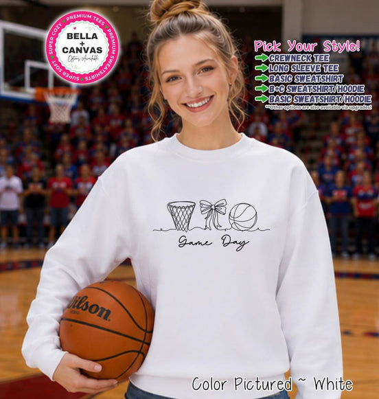May include: A white long-sleeve sweatshirt featuring a black line art graphic of a basketball hoop, a bow, and a basketball, with the text Game Day printed below. The design is centered on the chest of the garment, which is shown in a white color.
