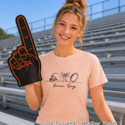 May include: A heather peach t-shirt featuring a black line art graphic of a football helmet, a bow, and a football, with the text 