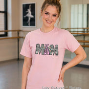 May include: A light pink short-sleeve t-shirt featuring the text MOM in a black and white checkered pattern. The letter O is replaced by a pair of pink ballet slippers with teal star accents and a pink bow. The shirt is a solid light pink color.