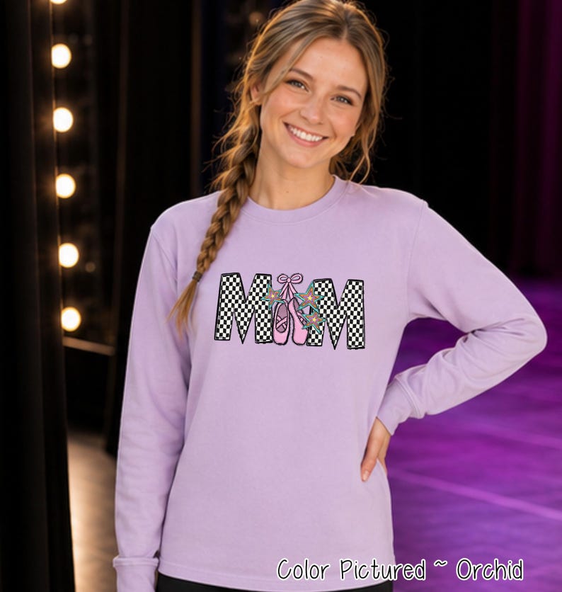 May include: A long-sleeved orchid-colored sweatshirt featuring the text MOM in a black and white checkered pattern. The letter O is replaced by a pair of pink ballet slippers with ribbons and small colorful star accents on the laces.