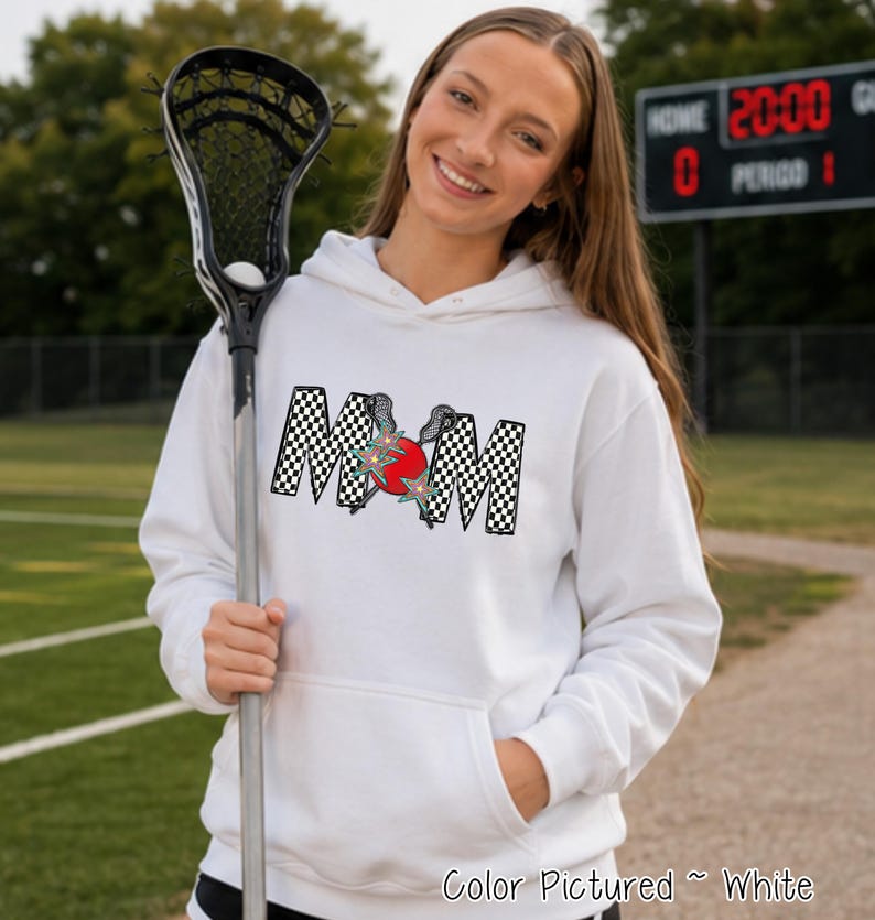 May include: A white hooded sweatshirt featuring a graphic on the chest with the word MOM in a black and white checkered pattern. The letter O is replaced by a red circle with two crossed lacrosse sticks and two teal star accents.