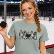 May include: A sage green short-sleeve t-shirt featuring a graphic print of the word MOM in a black and white checkered pattern. The letter O is replaced by a black hockey puck and two crossed hockey sticks, accented with colorful stars.