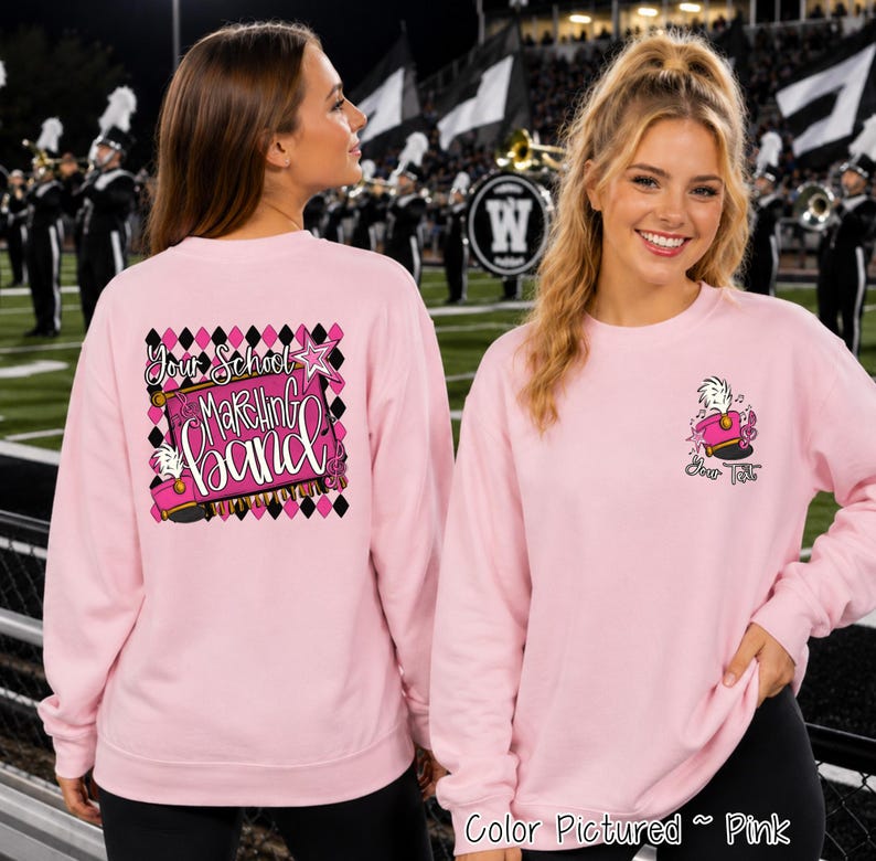 May include: A light pink long-sleeve sweatshirt featuring a graphic on the back with a black and pink diamond pattern, a pink marching band hat, and the text 