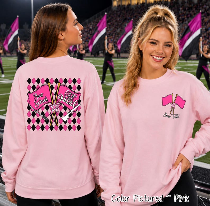 May include: A light pink long-sleeve sweatshirt featuring a color guard graphic. The back displays a black and pink diamond pattern with two crossed flags labeled 