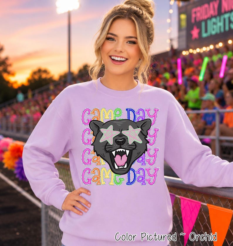 May include: A light purple crewneck sweatshirt featuring a graphic of a black panther head with star-shaped eyes. The text 