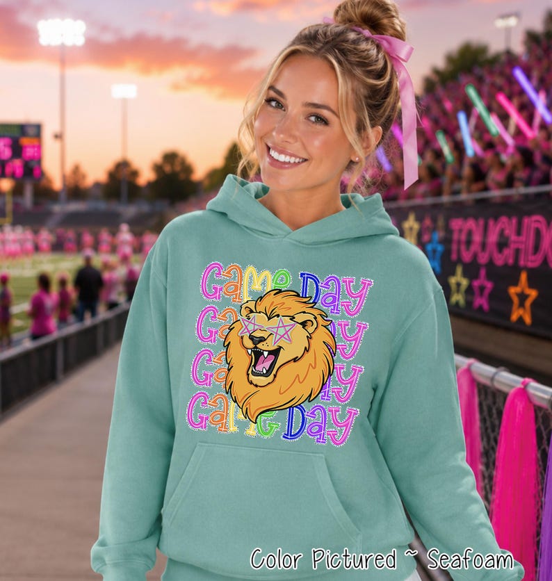 May include: A seafoam green hooded sweatshirt featuring a graphic of a lion with pink star-shaped glasses. The text 