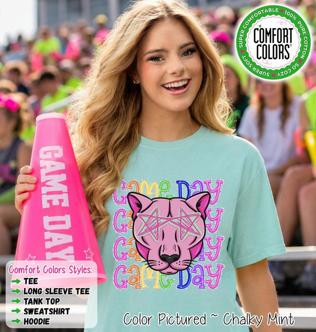May include: A light mint green t-shirt featuring a graphic of a pink panther face wearing star-shaped glasses, surrounded by the repeating text Game Day in colorful, patterned letters. A bright pink megaphone with the text Game Day is held nearby.