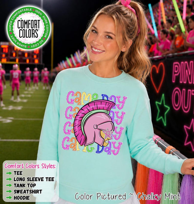 May include: A light mint green crewneck sweatshirt featuring a graphic of a pink Trojan helmet with a star over the eye, surrounded by the repeating text "Game Day" in colorful, outlined bubble letters. The garment has long sleeves and a ribbed collar.
