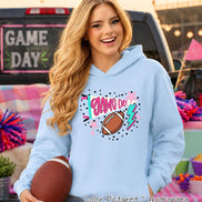 A light blue hooded sweatshirt featuring a graphic print on the chest with the text GAME DAY, a brown football, a pink megaphone, a pink star, and a teal lightning bolt. The hoodie is made of a soft fabric and has long sleeves.