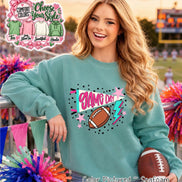 A seafoam green crewneck sweatshirt featuring a graphic print with the text GAME DAY in pink, a brown football, a light blue lightning bolt, and pink stars. A Comfort Colors chart shows options for a tee, long sleeve, sweatshirt, and hoodie.
