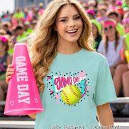 A chalky mint short-sleeve t-shirt featuring a graphic print of a yellow softball, a pink pennant with the text GAME DAY, a pink lightning bolt, and pink stars. A bright pink megaphone with the white text GAME DAY is also shown.